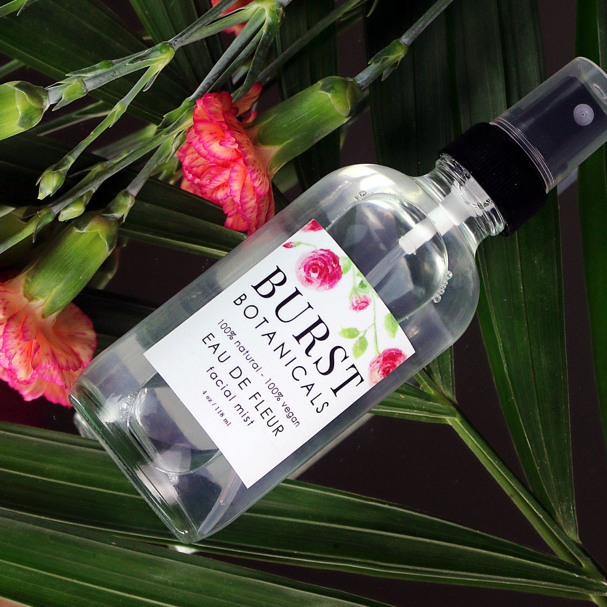 Facial mist bottle, clear glass with black cap, Burst Botanicals label, floral background