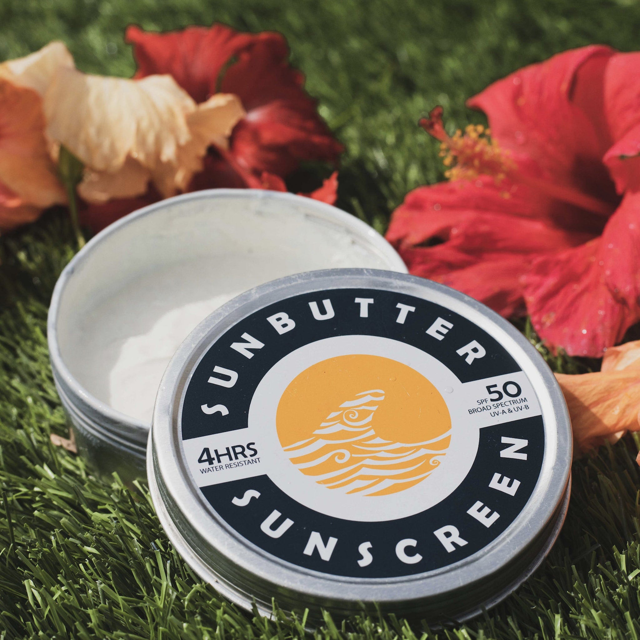 Sunscreen tin with white cream, black and white label, and silver metal container on green grass