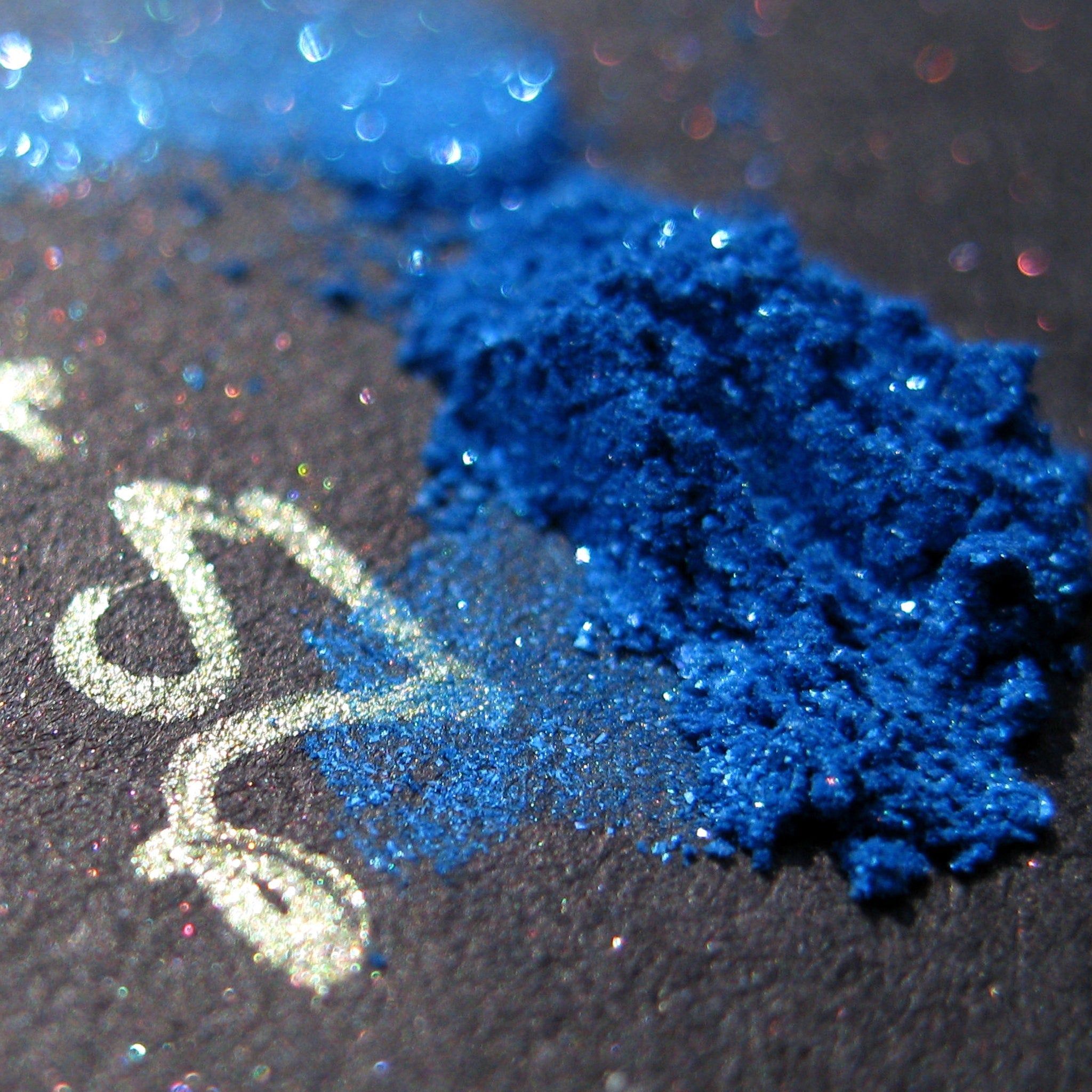 Open jar of royal blue loose mineral eyeshadow with iridescent turquoise shimmer and glitter particles.