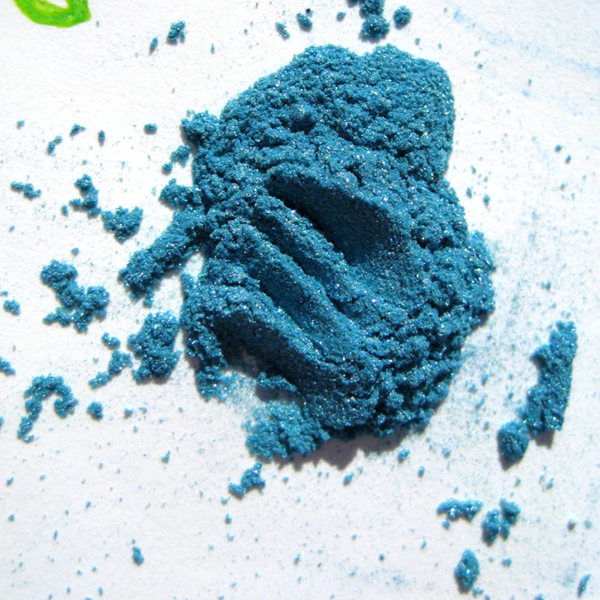 Hand applying iridescent turquoise blue loose eye shadow with teal and purple shimmer onto eyelid