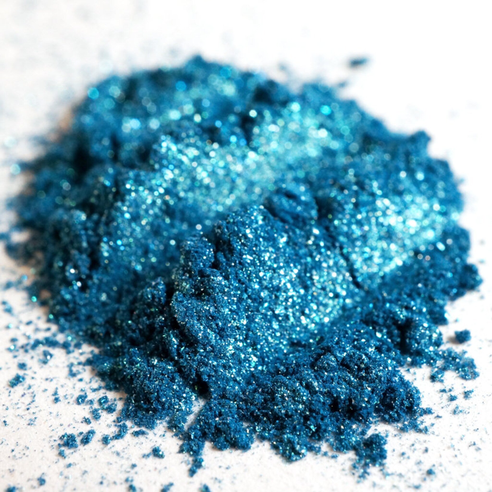 Hand applying teal shimmer loose eyeshadow with turquoise and green glitter using a makeup brush