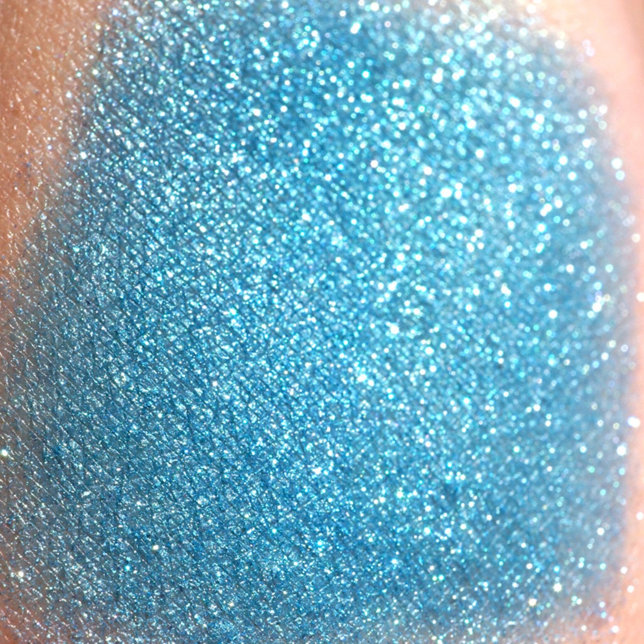 Side view of loose teal shimmer eyeshadow with turquoise and green glitter in a sifter jar