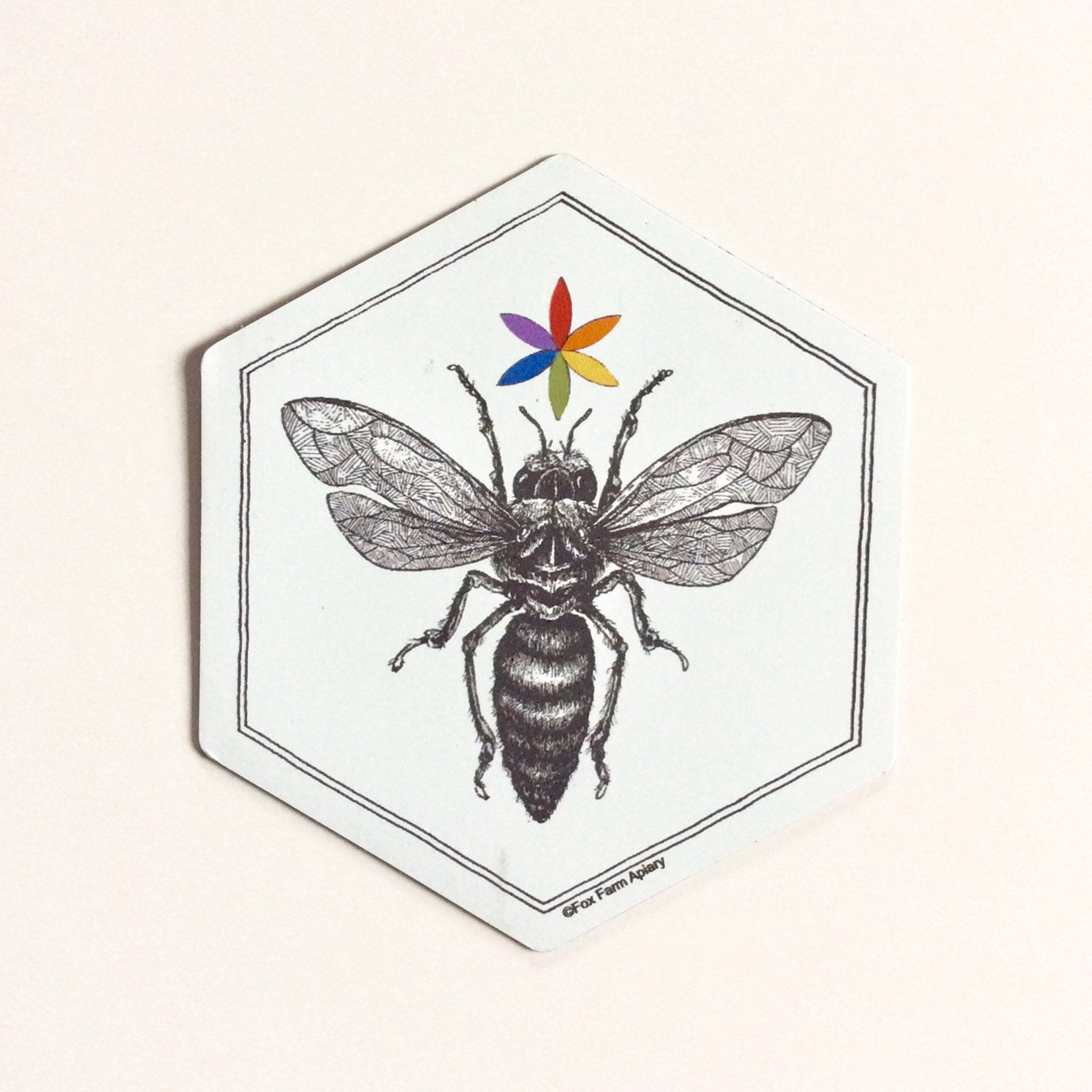 Bee illustration with black and white details, rainbow flower, and hexagonal shape with Fox Farm Apiary text