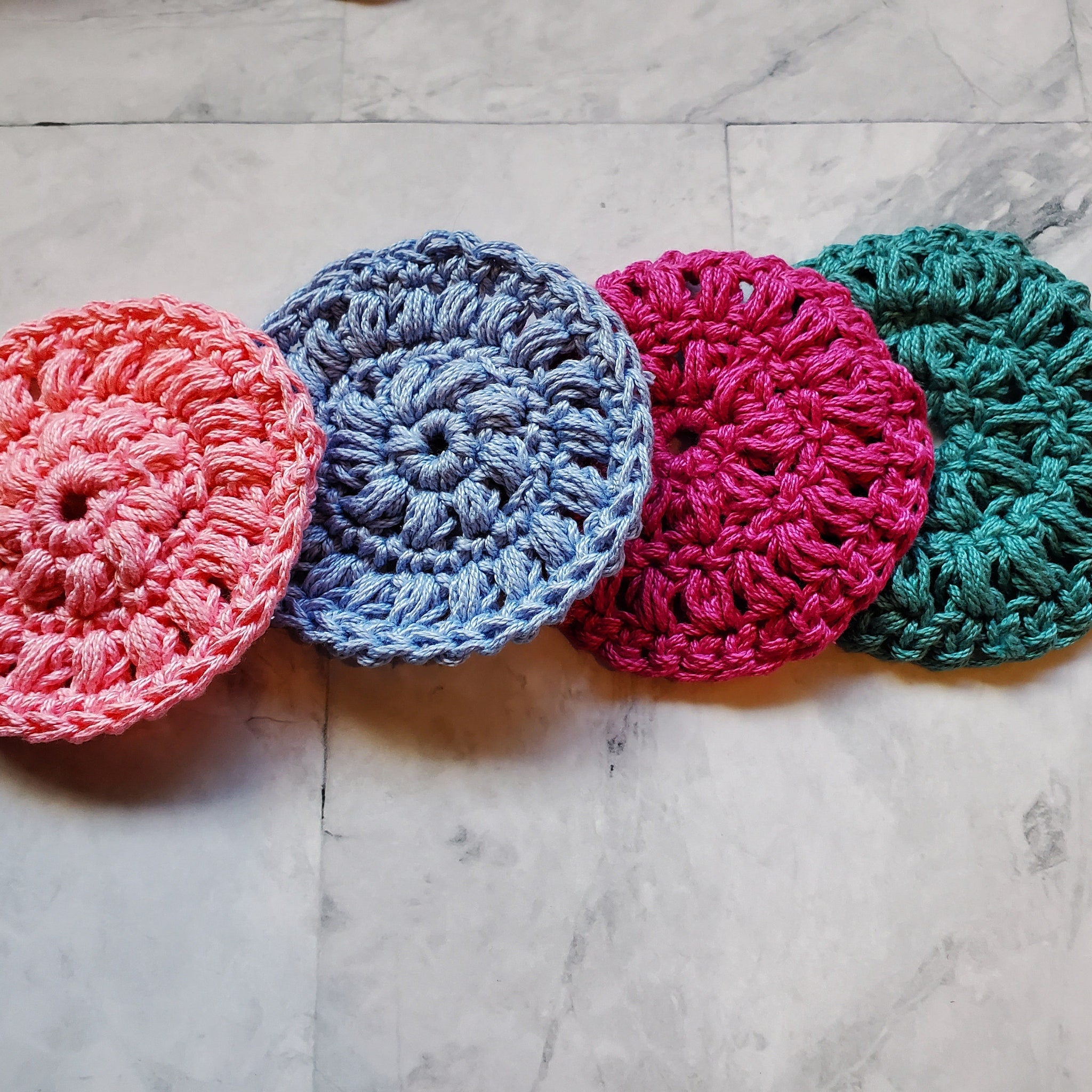 Crochet washcloths in pink, blue, red, and green, with a round pattern and visible texture