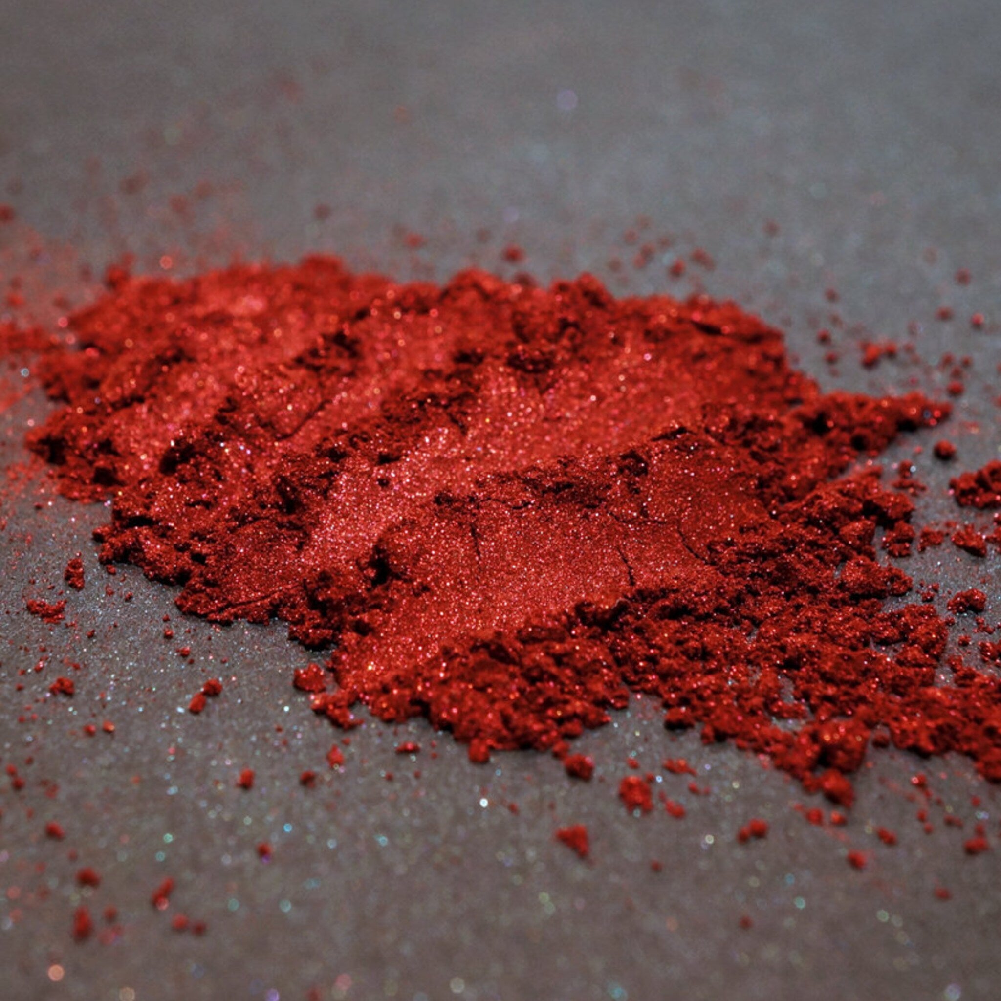Open jar of blood red metallic loose mineral eyeshadow with shimmer particles spilling onto black surface
