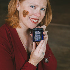 Facial Exfoliant jar with blue and black label held by woman in red top, Unbelievable Skincare brand visible