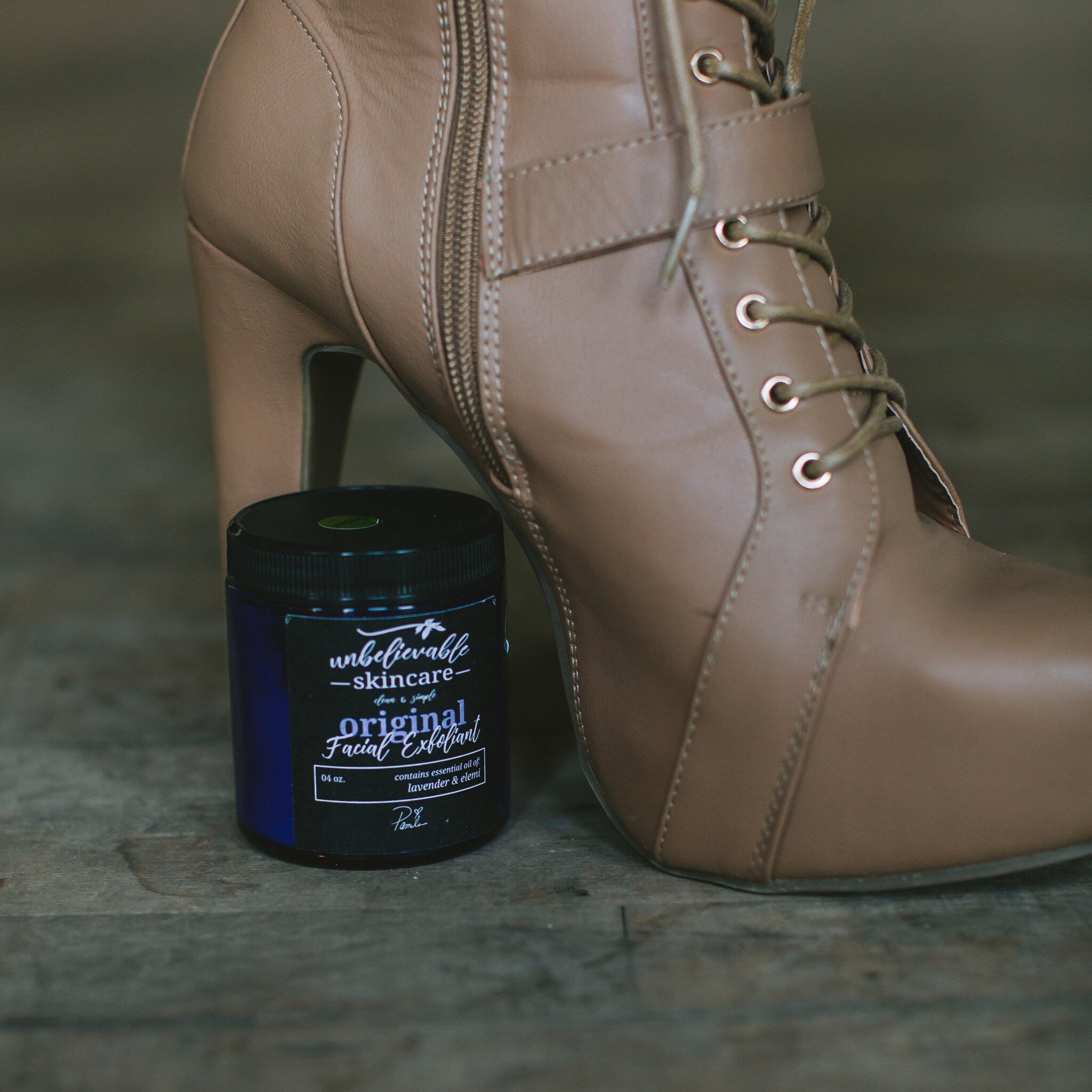 Facial Exfoliant jar with blue label, black lid, and tan leather boot in background