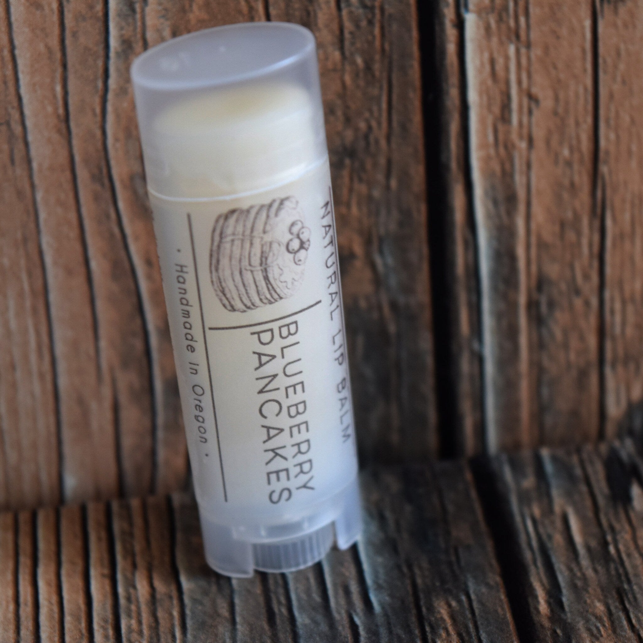 Lip balm in a white tube with Blueberry Pancakes label, on a wooden background.