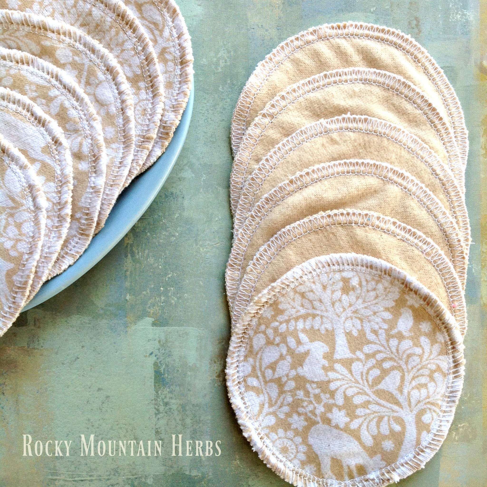Nursing pads with beige fabric, white floral pattern, and white stitched edges, by Rocky Mountain Herbs
