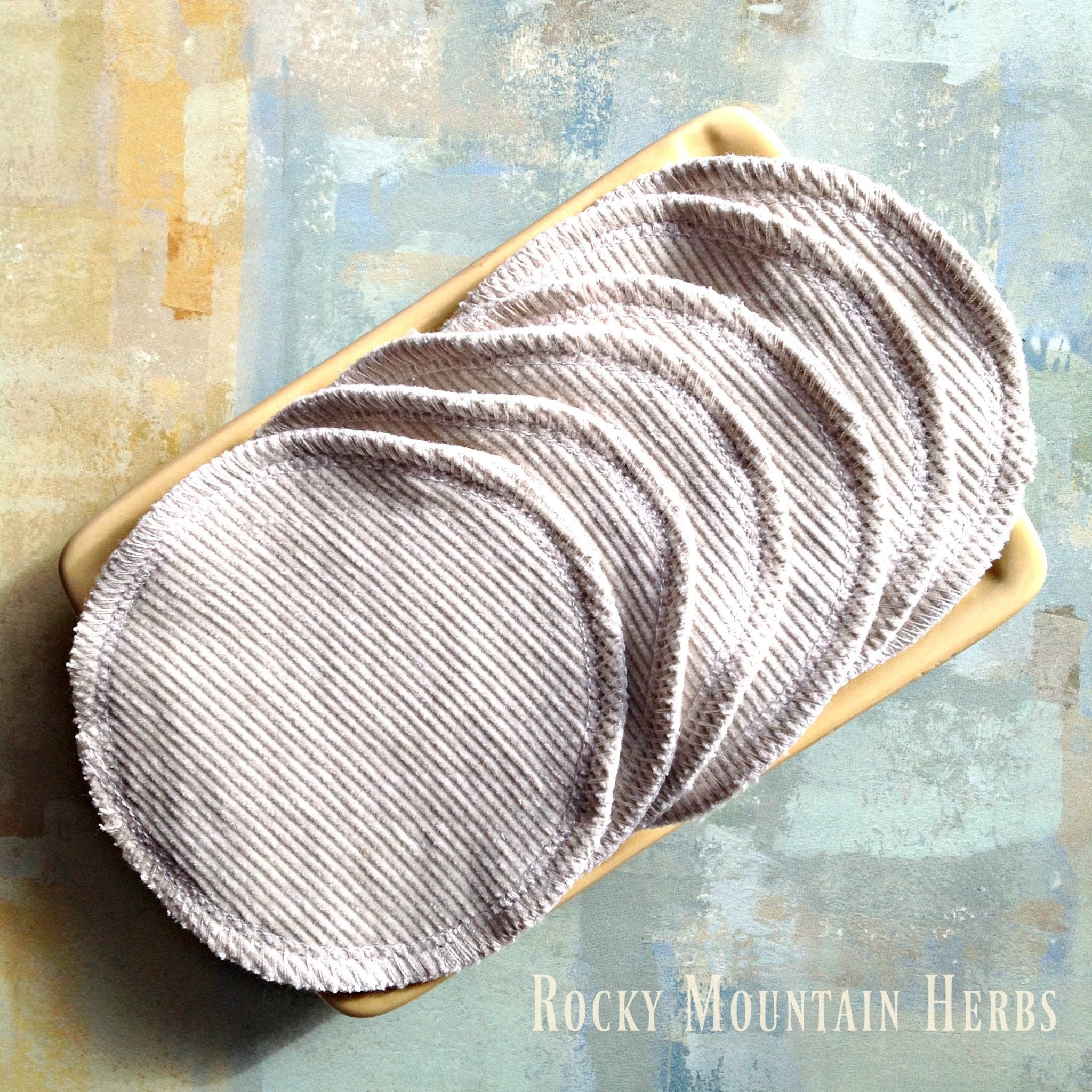 Reusable facial rounds in gray corduroy fabric, stacked in a beige tray, Rocky Mountain Herbs brand