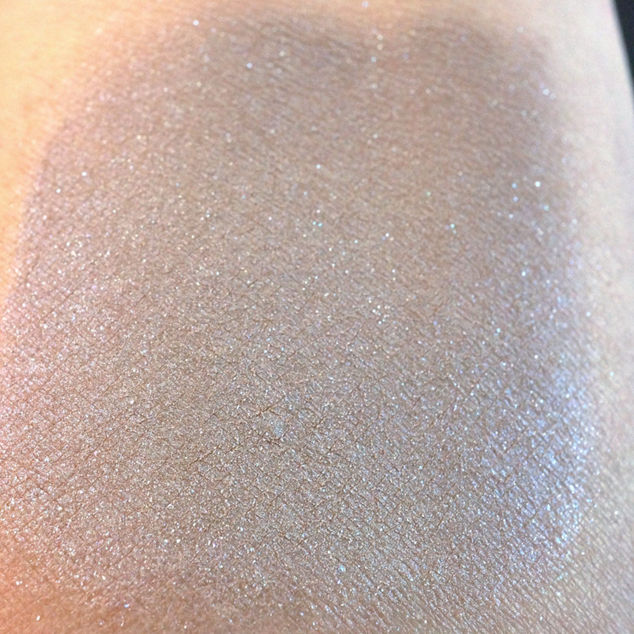 Side view of taupe eyeshadow pan showing beige base with silver and iridescent blue shimmer particles