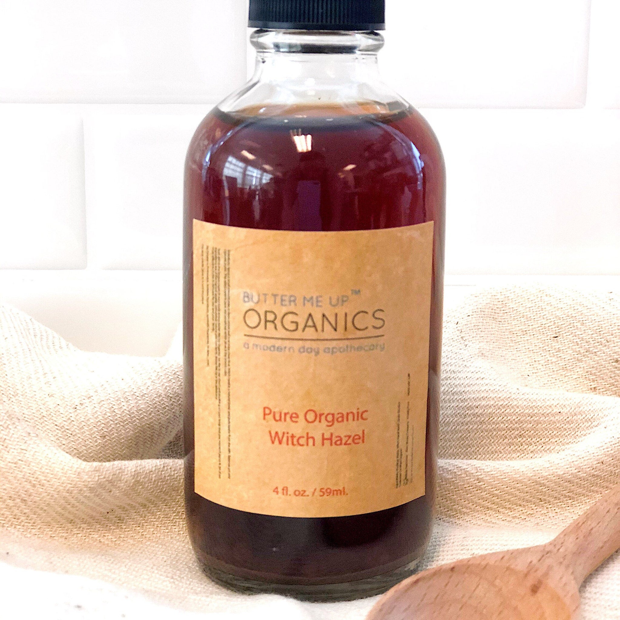Witch Hazel bottle with brown liquid, tan label, black cap, and "Butter Me Up Organics" text