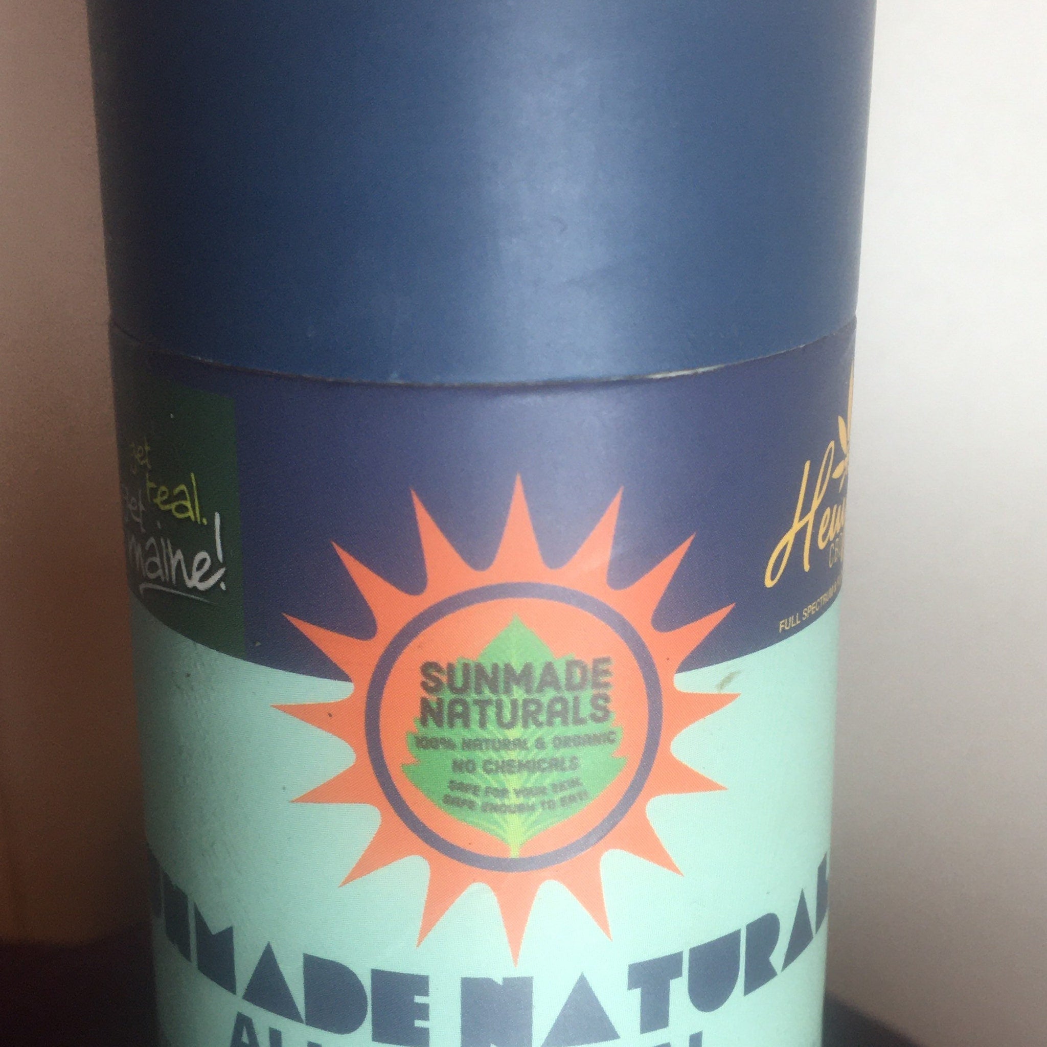 Sunmade Naturals container, blue and teal cylindrical packaging with orange sun logo and text