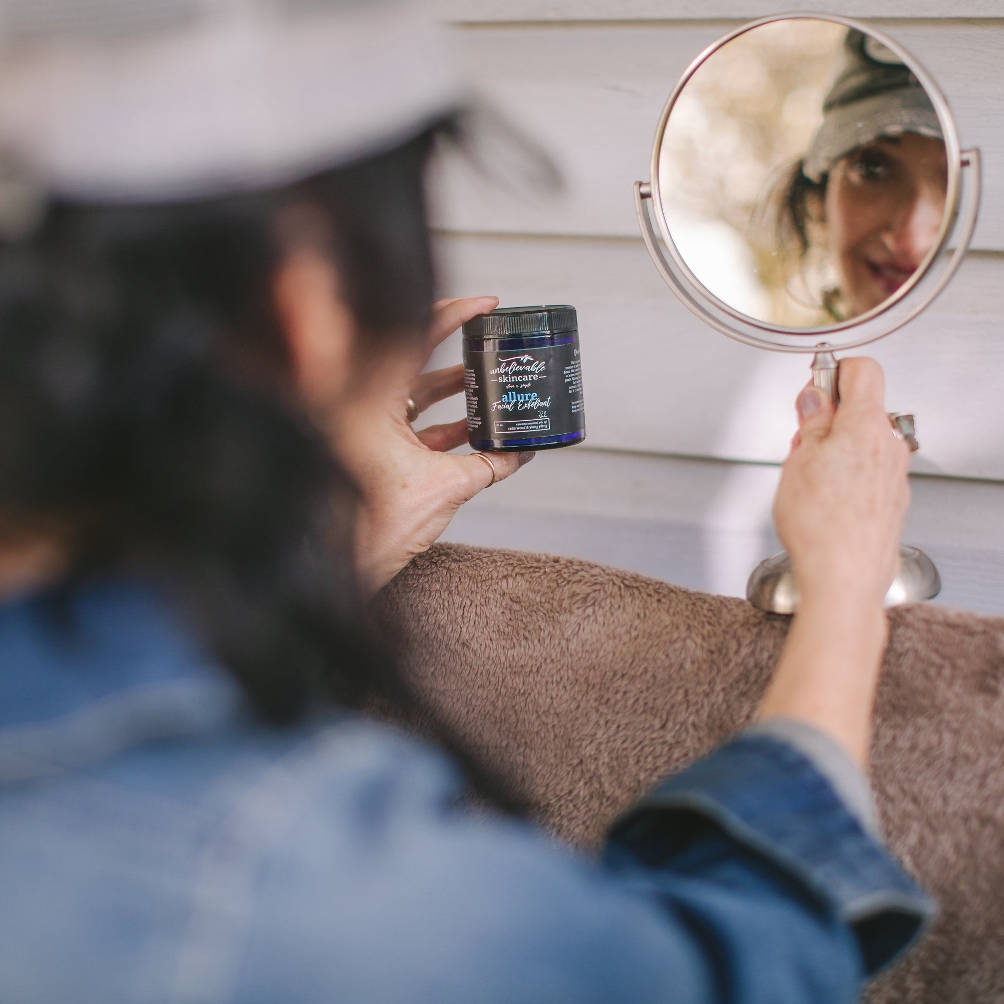 Facial Exfoliant jar with dark blue label, black lid, and "Unbelievable Skincare" branding being held near mirror