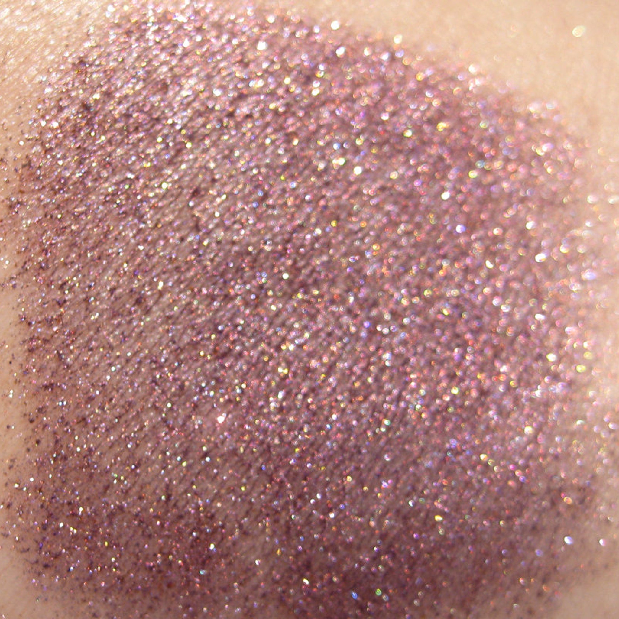 Side view of warm metallic purple eyeshadow pan with iridescent copper shimmer and glitter particles catching light