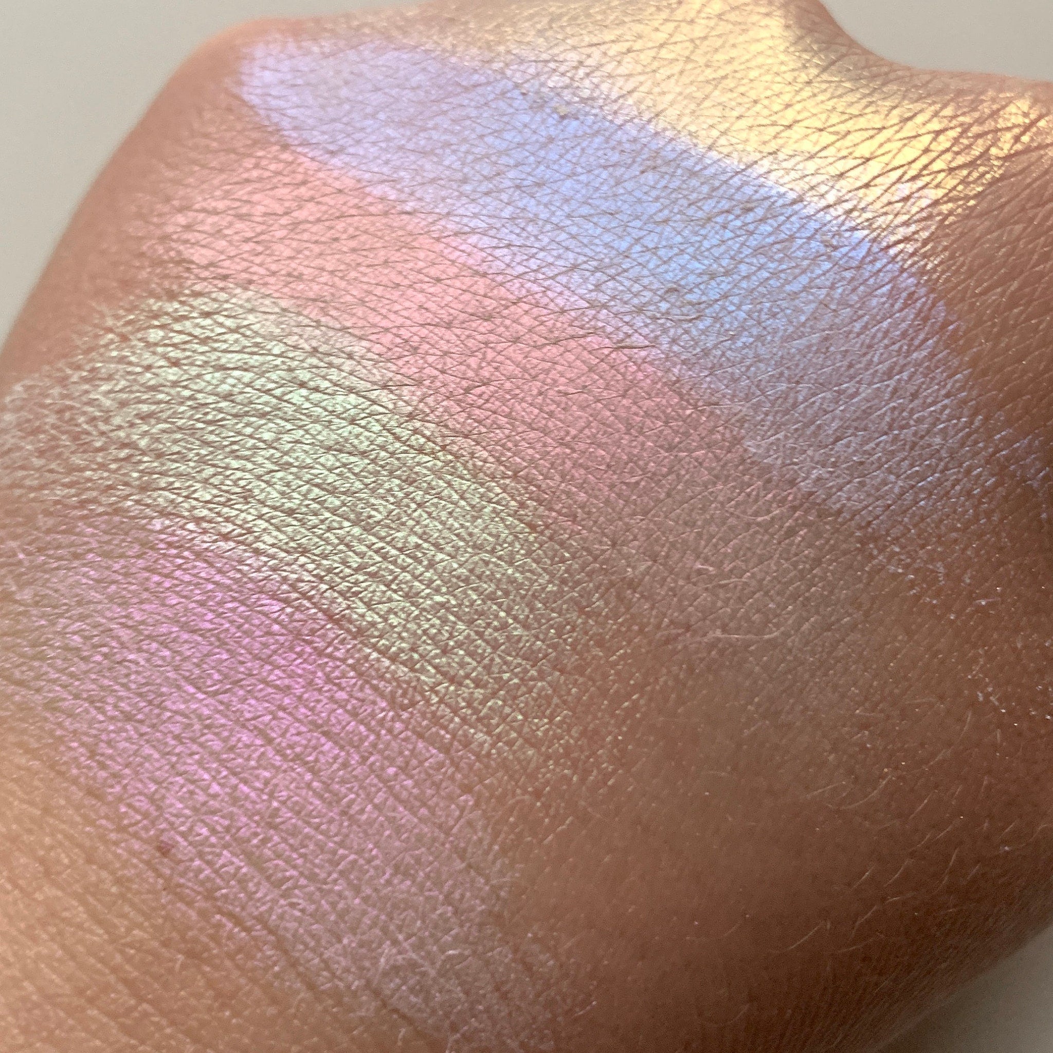 Iridescent makeup swatch with pink, blue, and yellow shimmer on skin