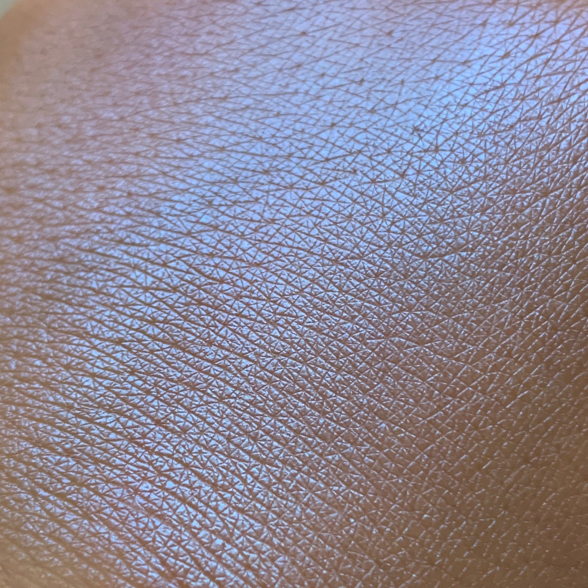 Close-up of fingertips applying shimmering blue eye shadow to eyelid with soft blending brush