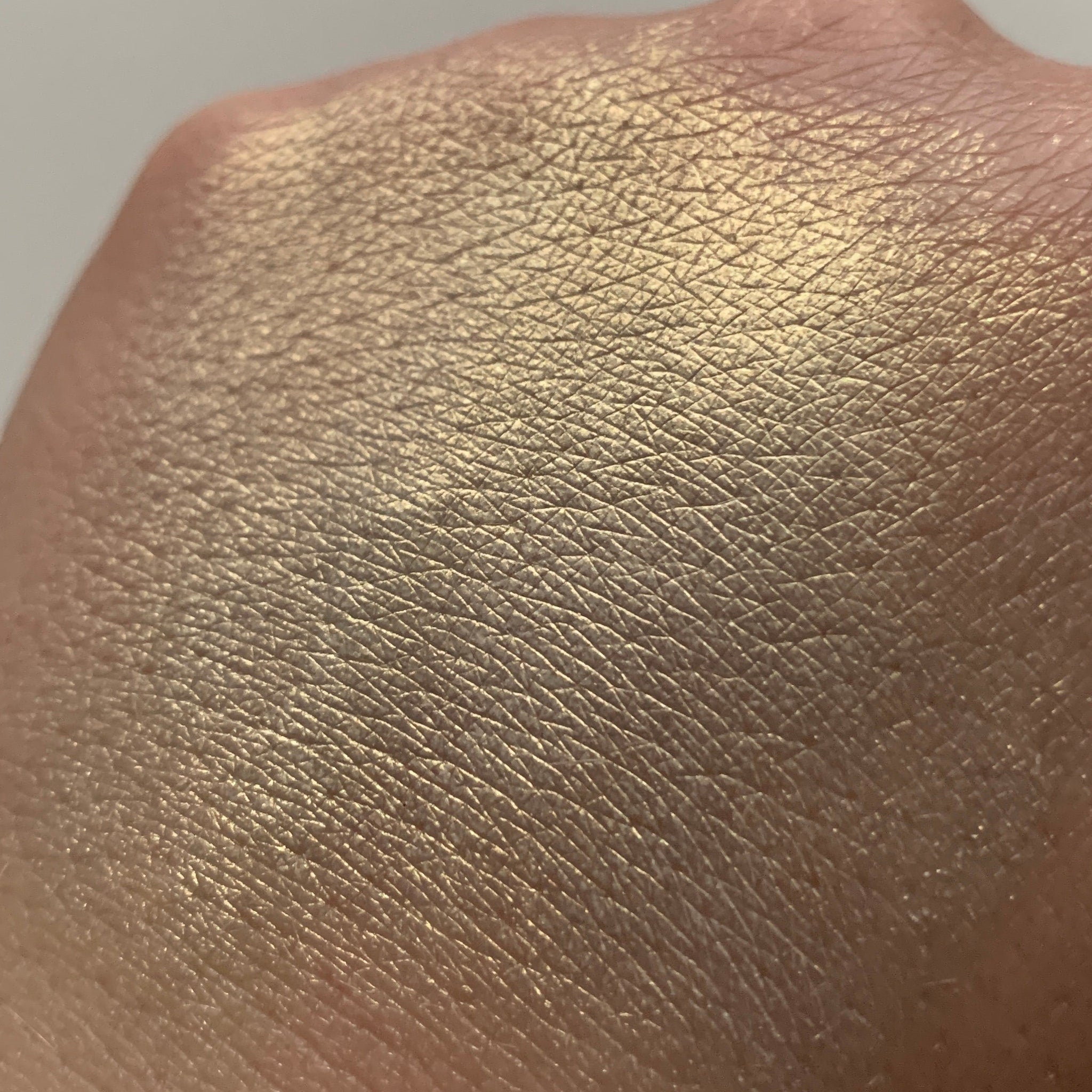 Gold eyeshadow swatch on skin, showing metallic shimmer and textured skin details