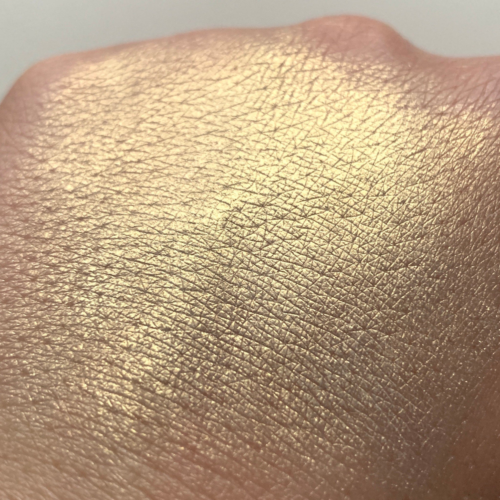 Gold shimmer swatch on skin, showing textured surface and light reflection
