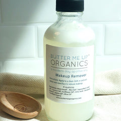 Makeup remover in glass bottle with black cap, white label, and wooden spoon on fabric