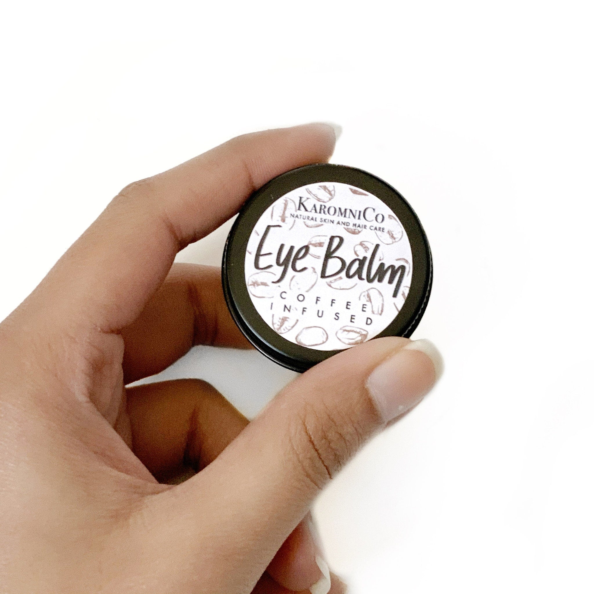 Eye balm tin held in hand, black metal container with white label, coffee infused text
