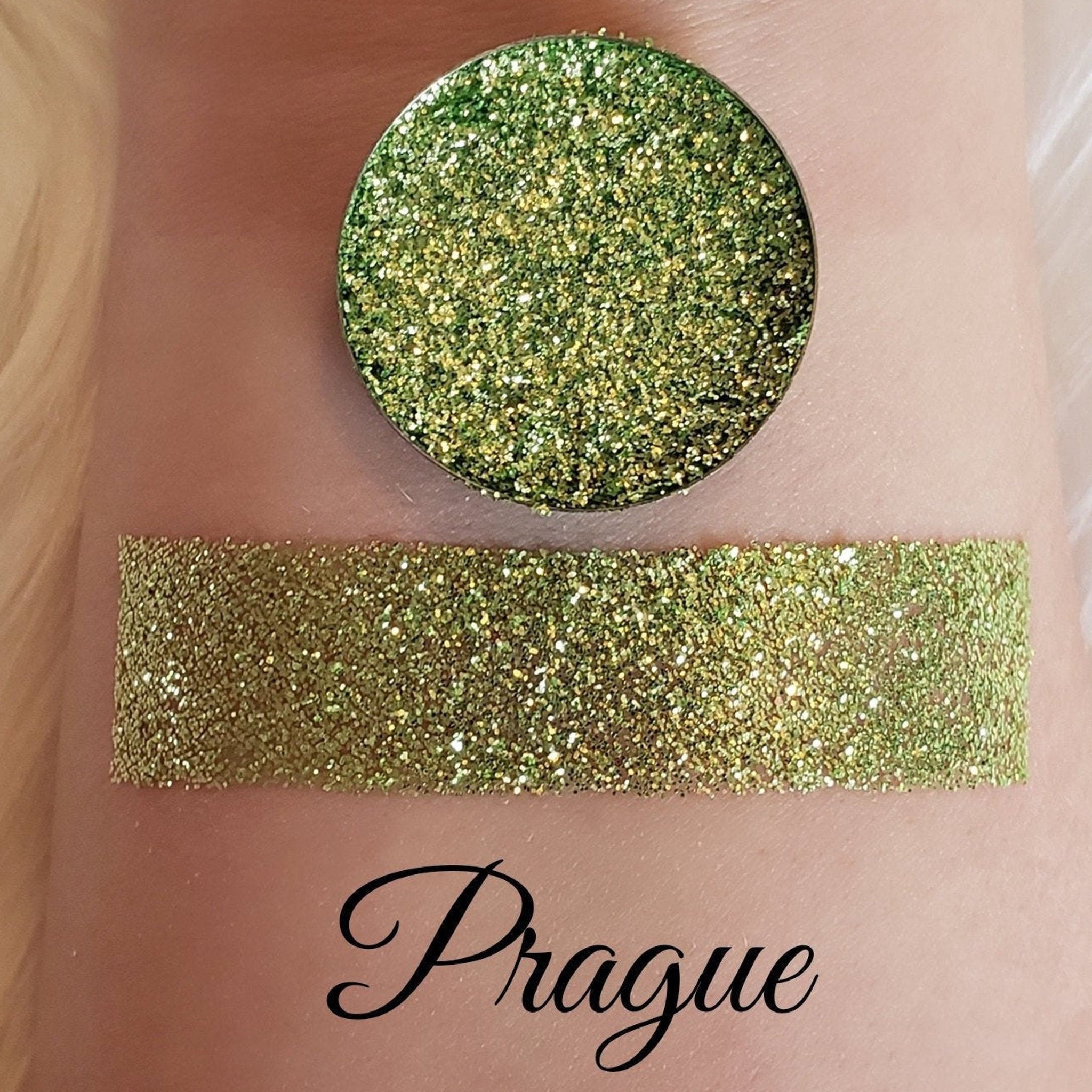 Glitter eyeshadow swatch with green and gold glitter, applied on skin, "Prague" text