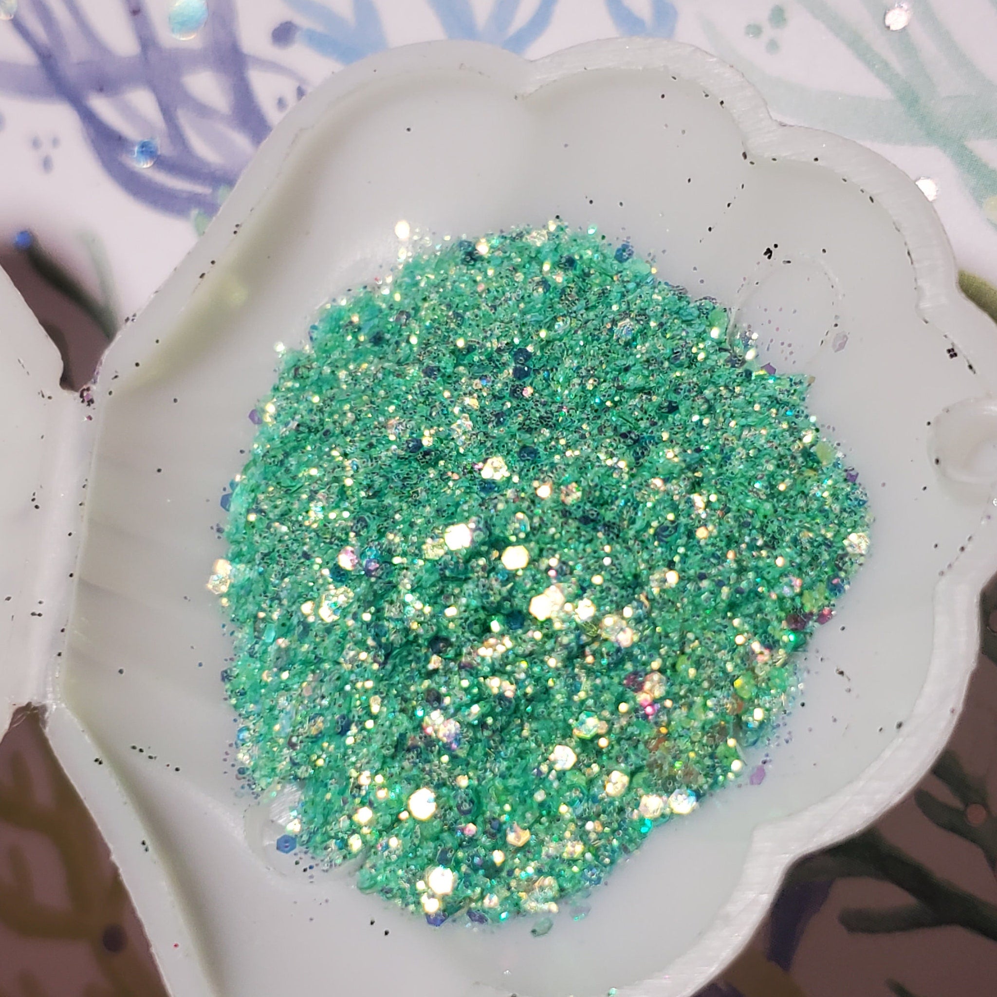 Square turquoise glitter gel eyeshadow pot with gold lid on marble surface