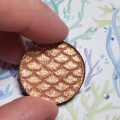 Close-up of Dobby Eye Shadow pan showing shimmering bronze powder with smooth, blendable texture