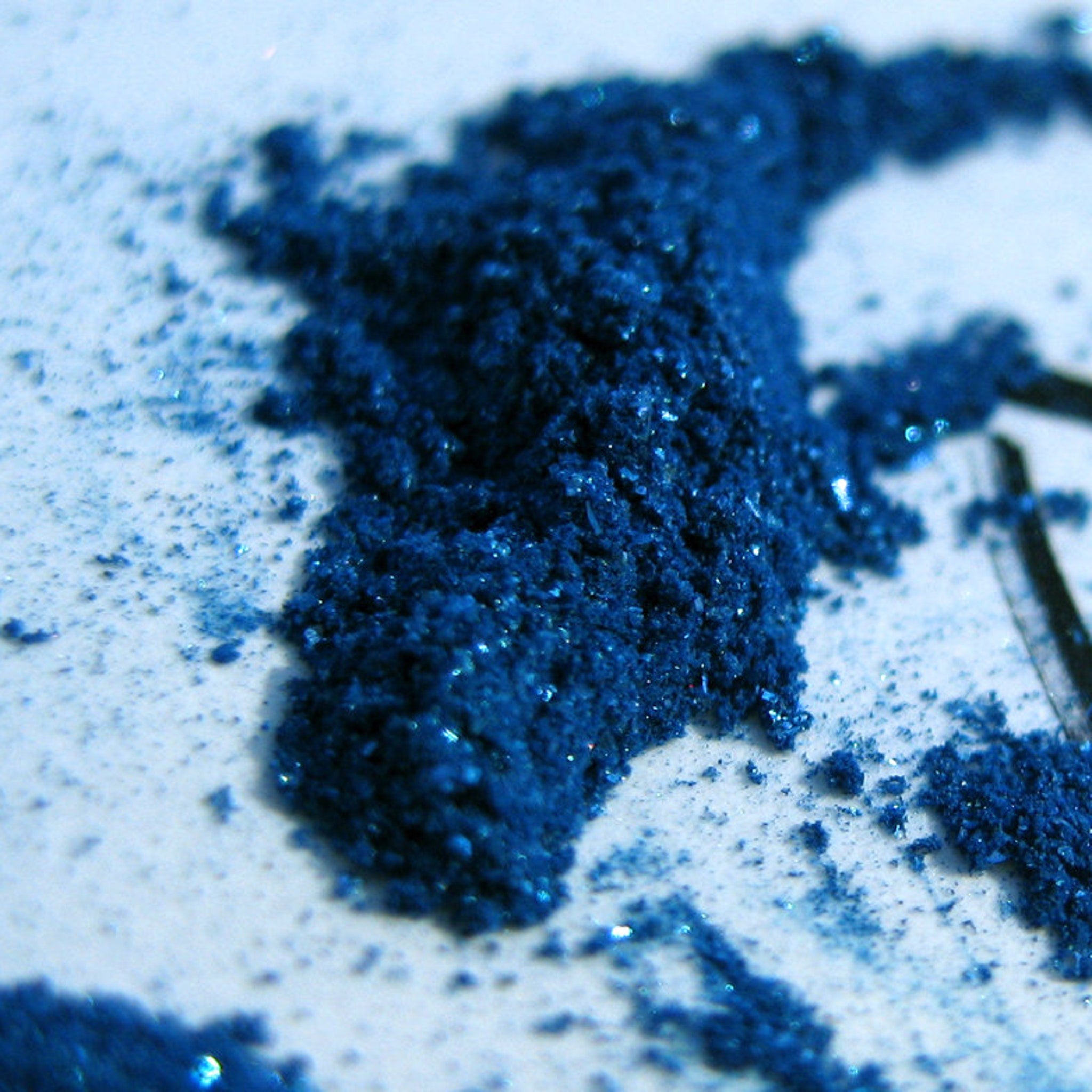 Close-up of iridescent turquoise shimmer and glitter particles in royal blue loose mineral eyeshadow