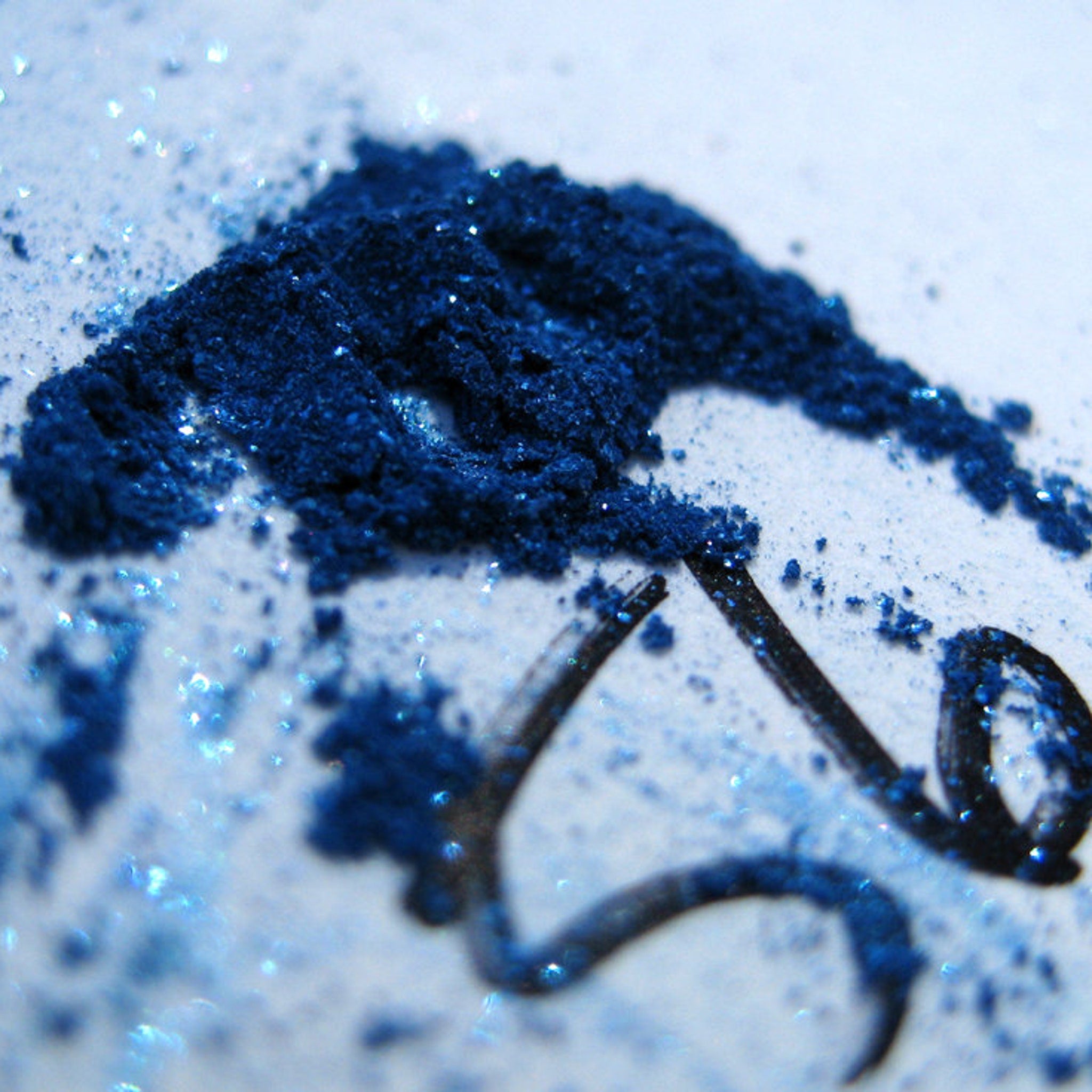 Hand applying iridescent royal blue loose mineral eyeshadow with turquoise shimmer onto eyelid