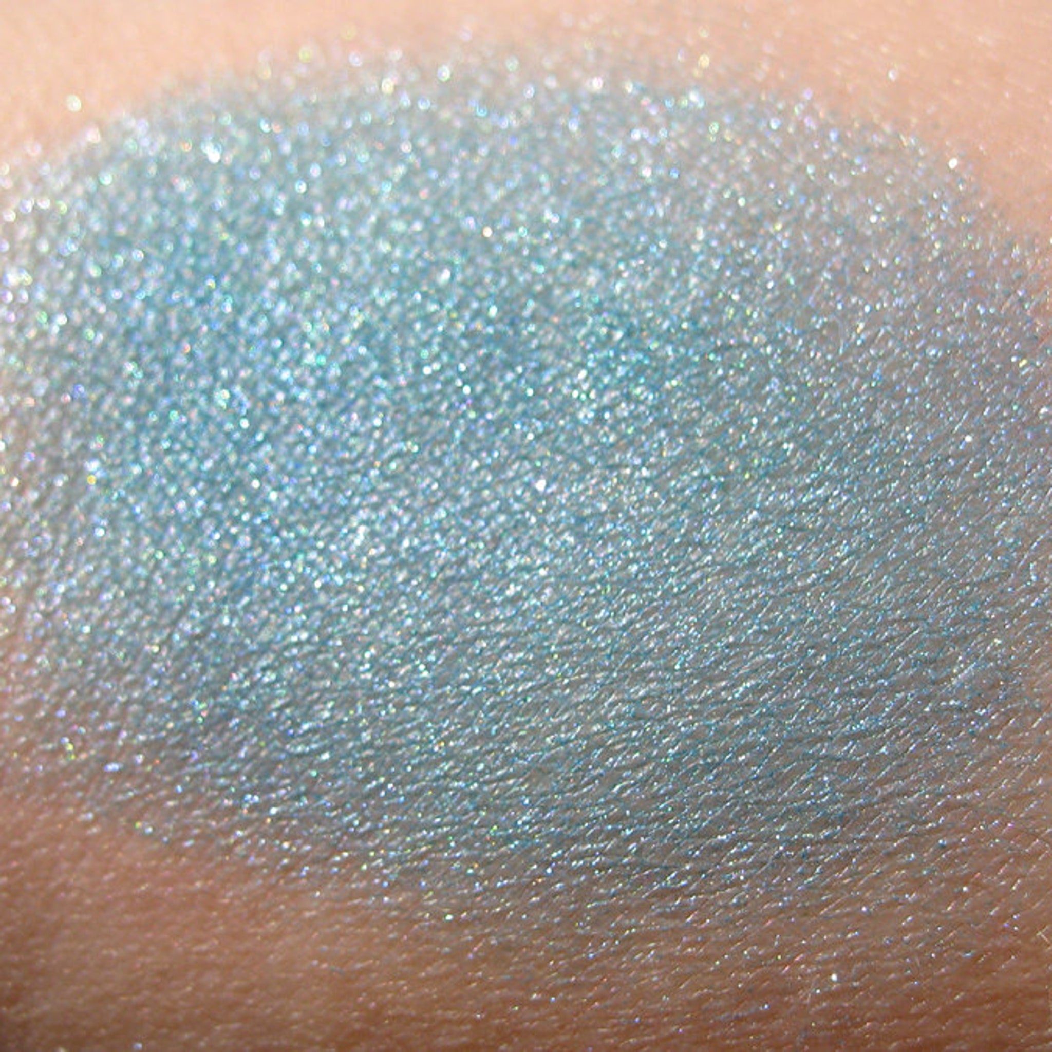 Side view of loose turquoise blue eye shadow with teal, iridescent aqua, and purple shimmer in mineral pigment jar
