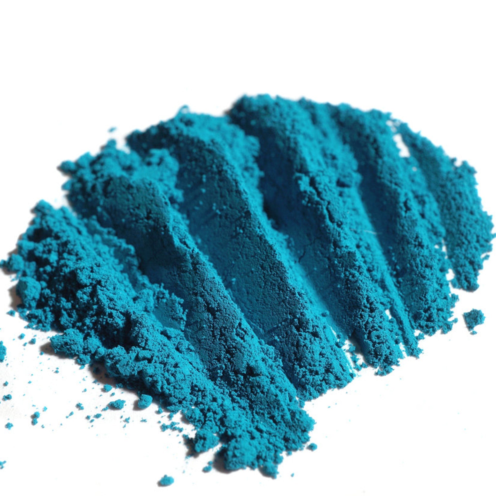 Close-up of matte teal loose eyeshadow powder with dark peacock turquoise hue, showcasing fine pigment texture