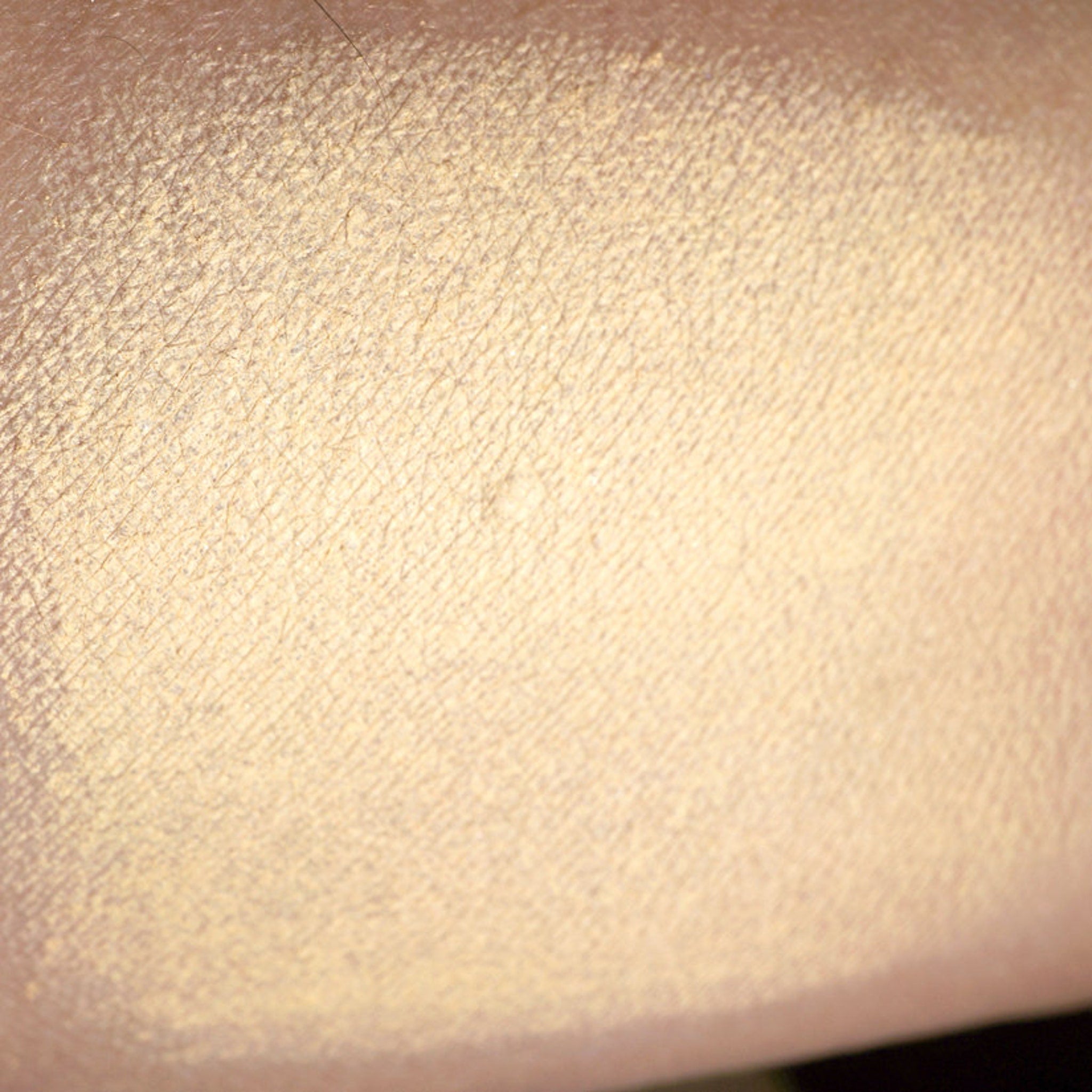Side view of matte pastel peach loose pigment eyeshadow in a sifter jar with spilled powder on surface
