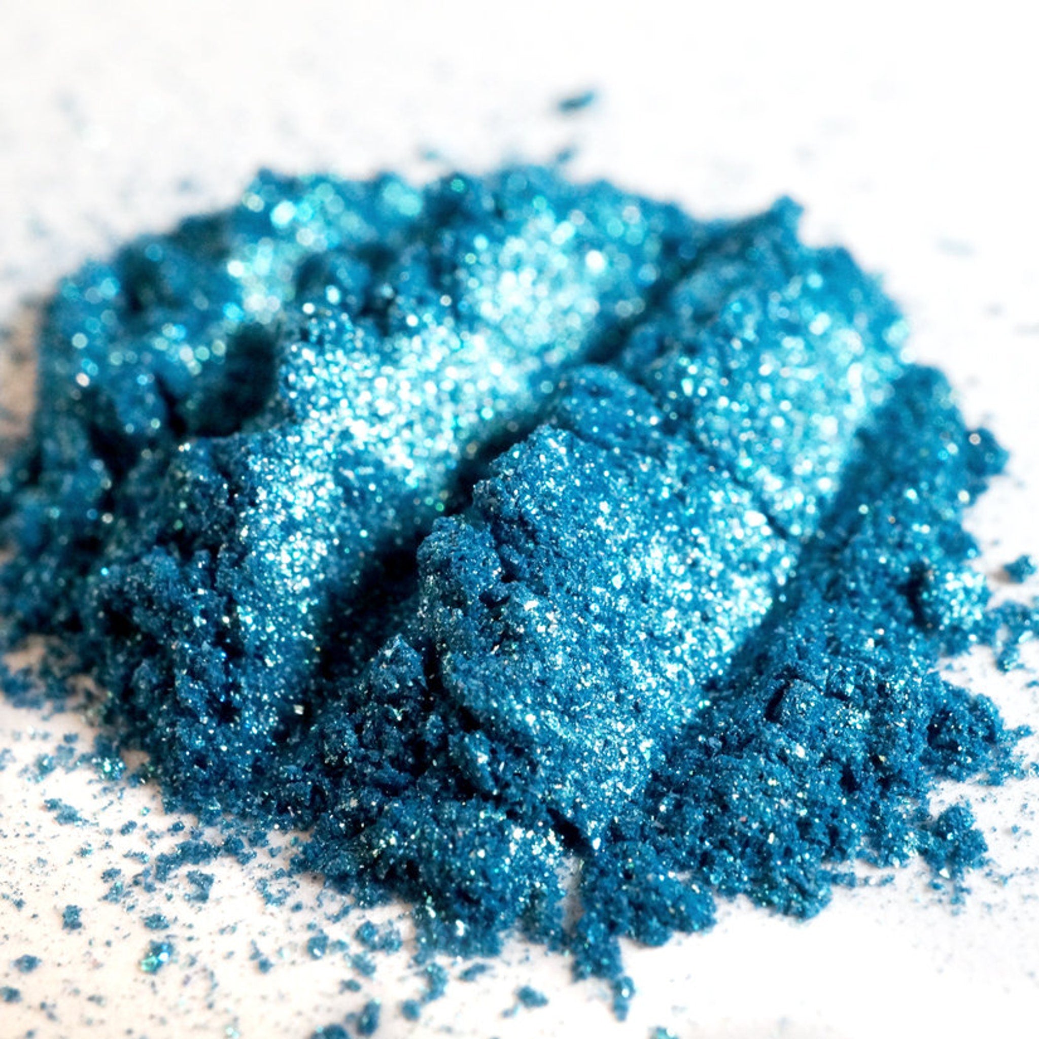 Close-up of teal shimmer loose mineral eyeshadow with turquoise and green glitter particles sparkling in light
