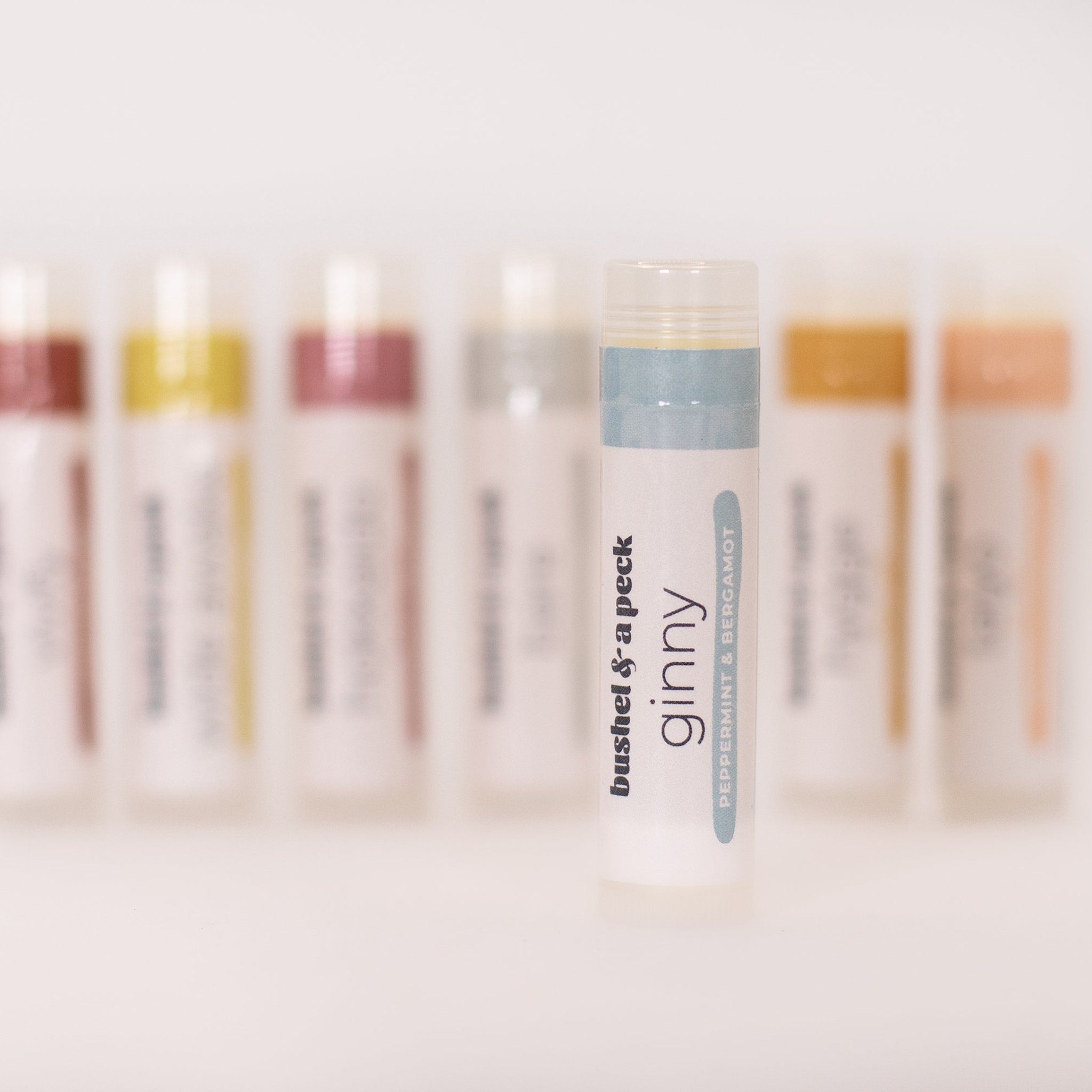 Lip balm tube with white, blue, and clear plastic, "bushel & a peck ginny" text visible