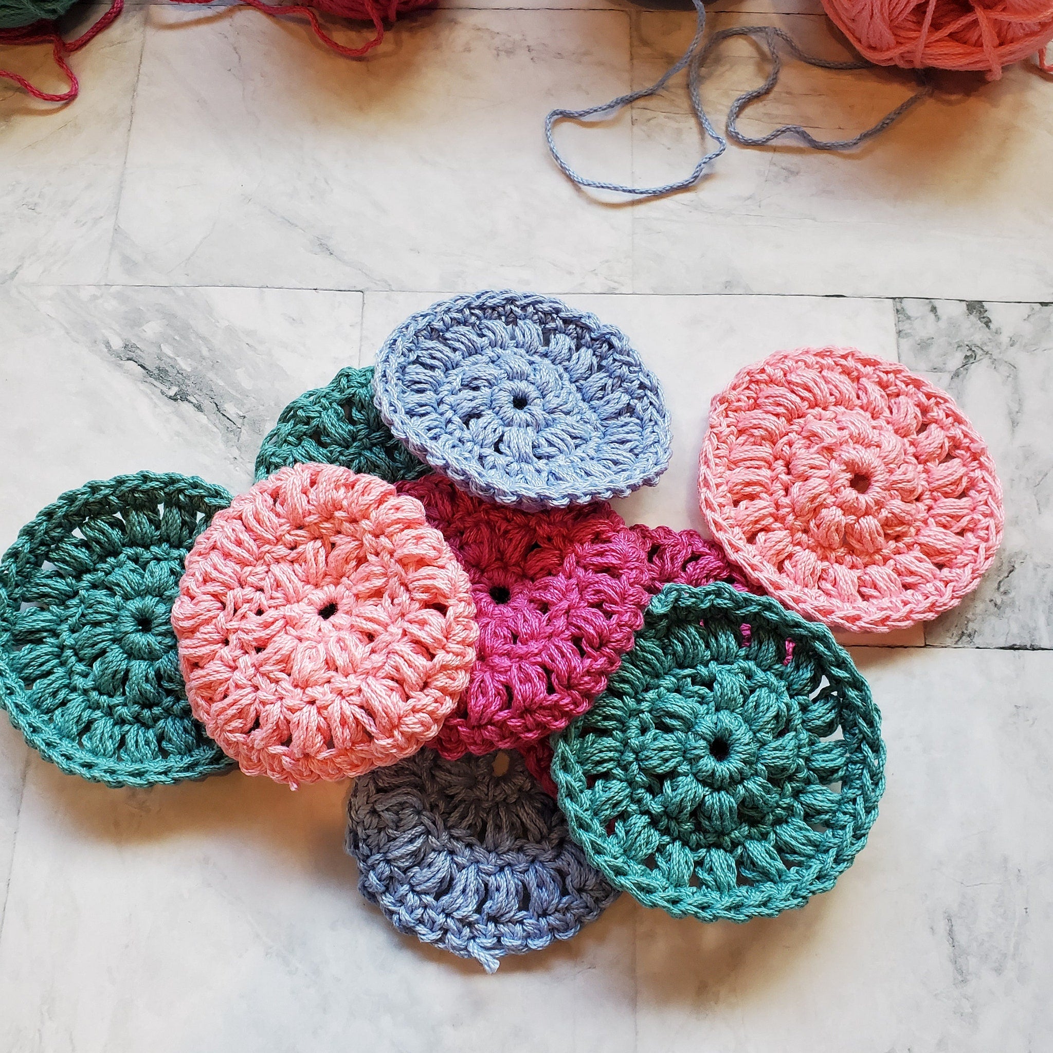 Crochet washcloths in various colors, round shape, handmade cotton texture, scattered on surface