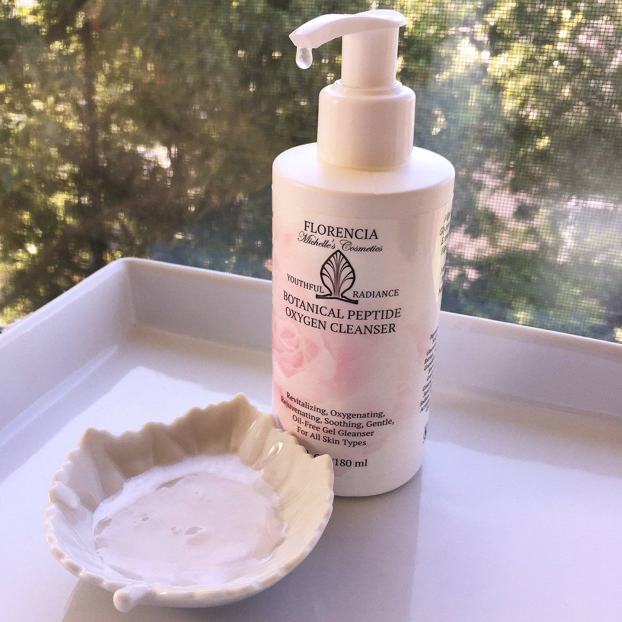 Oxygen cleanser bottle, white and pink with pump, next to leaf-shaped dish with liquid inside