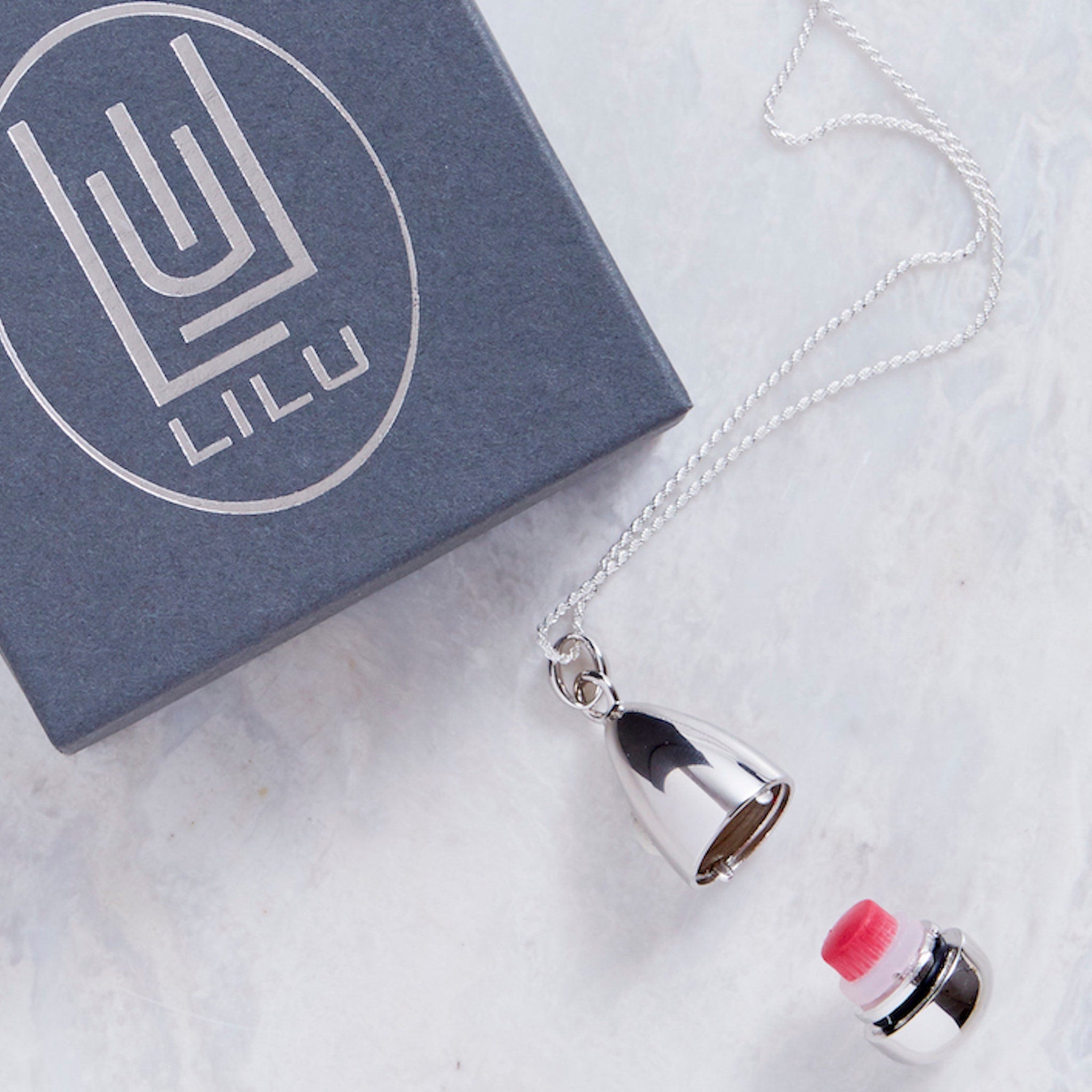 Necklace with silver chain and pendant, LILU logo on gray box, and red and white object