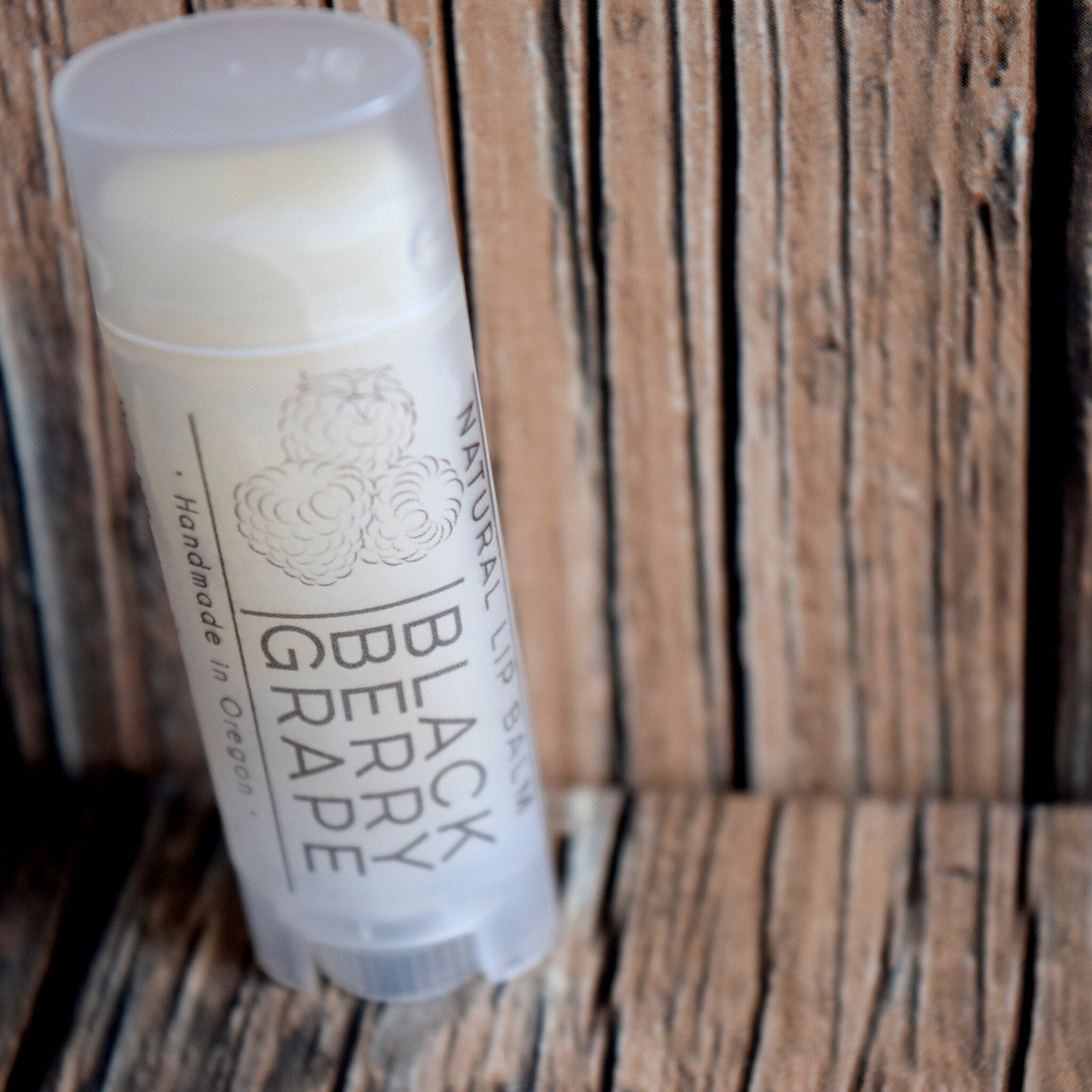 Lip balm tube with white label, light gray text, and wooden background