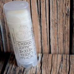 Lip balm tube with white label, light gray text, and wooden background