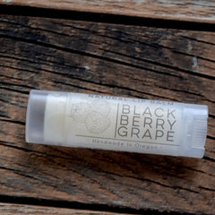 Lip balm in clear plastic tube with "Black Berry Grape" text on white label, on wood surface