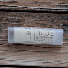 Lip balm in clear tube with white label, "Blue Raspberry Slushie" text, on wood grain background