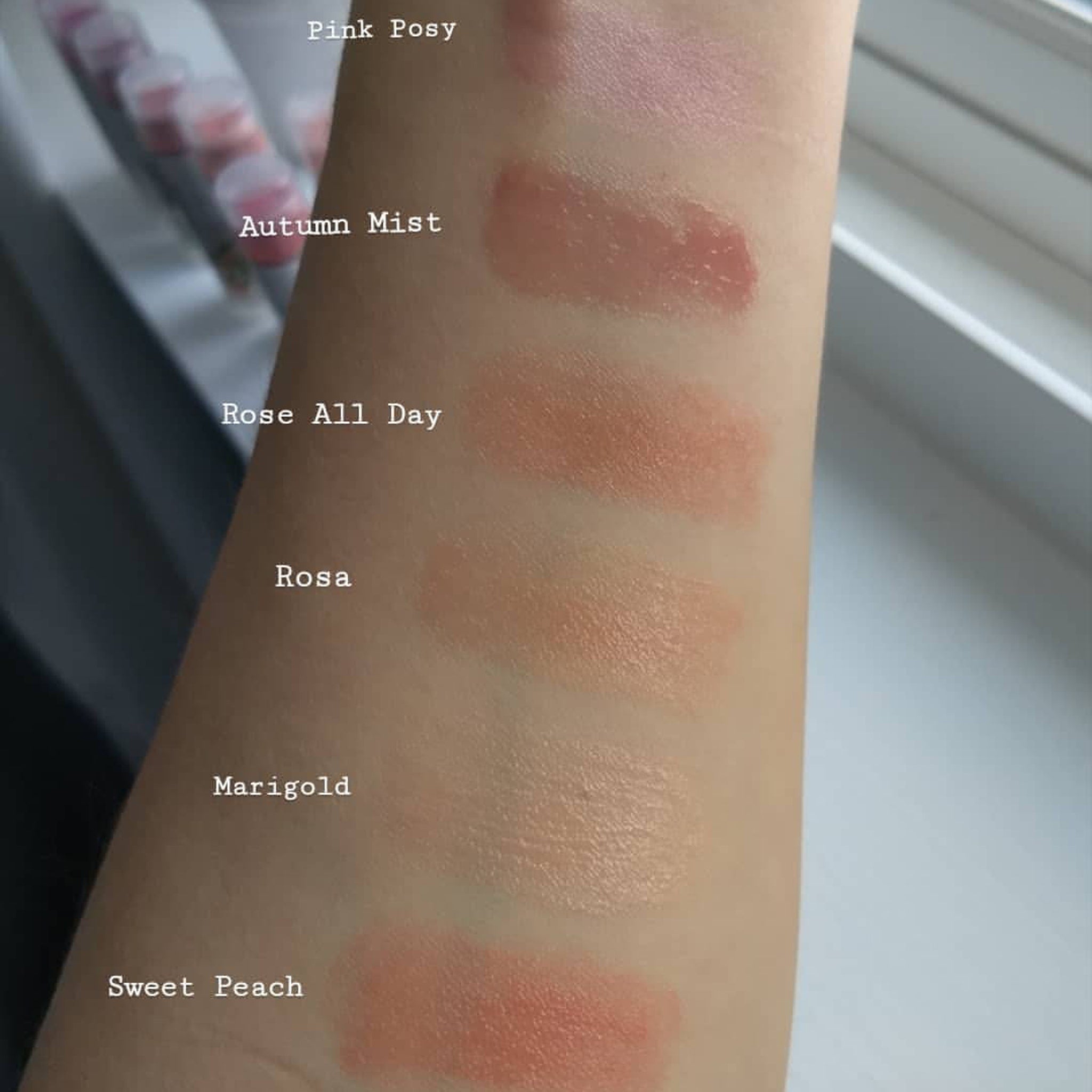 Lipstick swatches on arm, various shades of pink and peach, showing color and texture