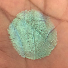 Green iridescent textured makeup swatch on skin, showing brush strokes and blue highlights
