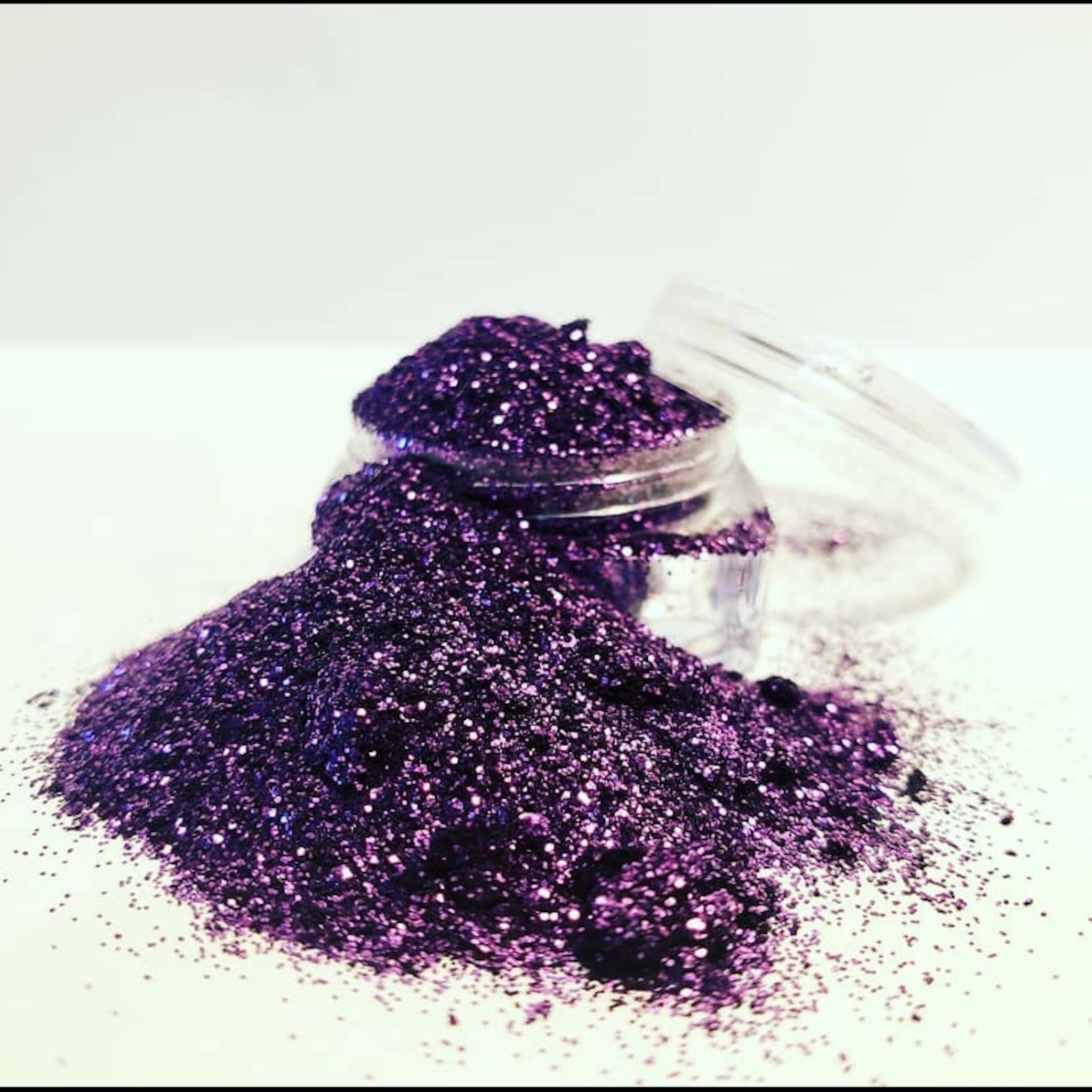 Purple glitter in a jar, with sparkly texture and clear lid on white surface