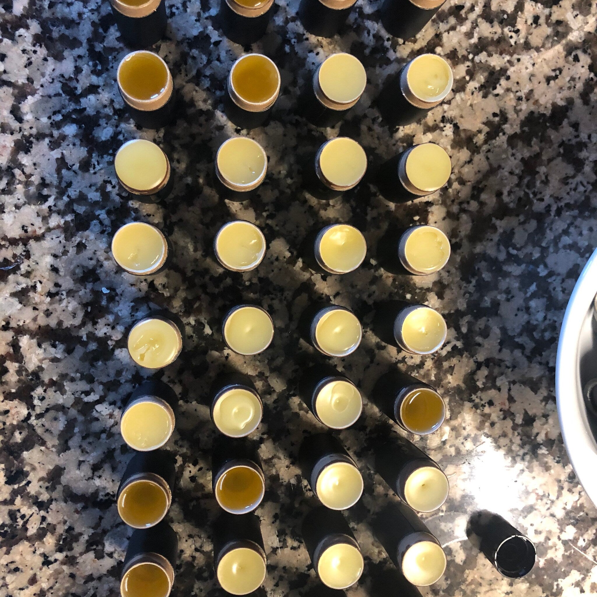 Lip balm tubes with yellow balm, black tubes, and light brown rim detail on a dark surface