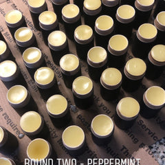 Lip balm containers with yellow balm, black base, and silver rim, arranged on cardboard