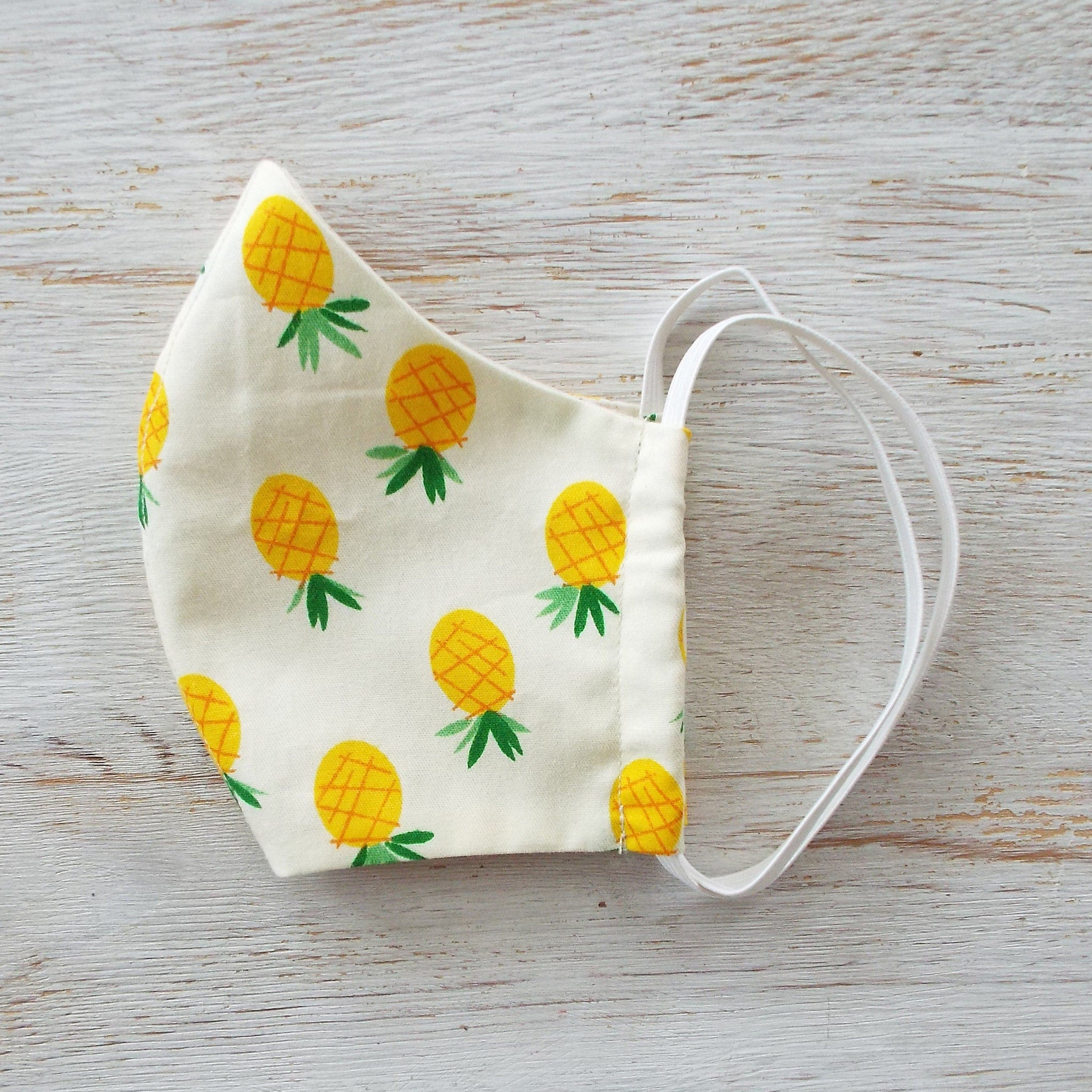 Side view of a folded cotton face mask showing adjustable ear loops and multi-layer fabric texture in neutral tones