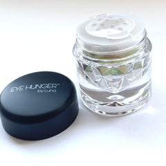 Eye shadow jar, clear glass with faceted design, black lid with text, and green powder inside