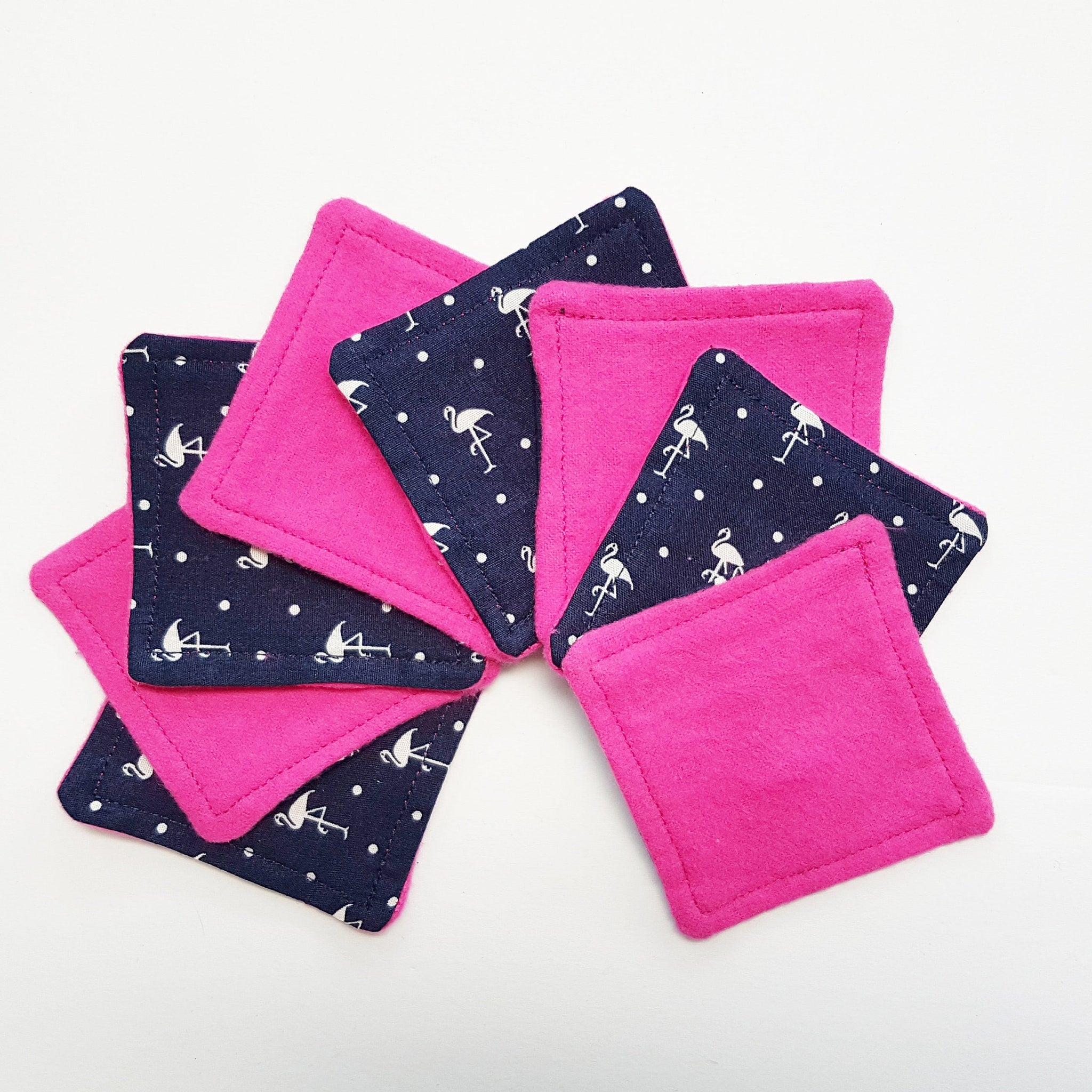 Square fabric coasters in pink and navy with flamingo pattern, stacked on white surface